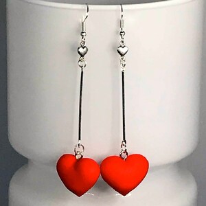 May include: A pair of dangle earrings with silver hooks and long silver chains. Each chain is topped with a small silver heart and ends with a large red heart charm.