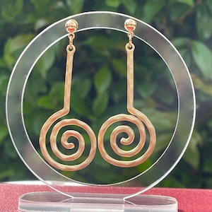 May include: A pair of gold-tone dangle earrings with a spiral design. The earrings are displayed on a clear acrylic stand.