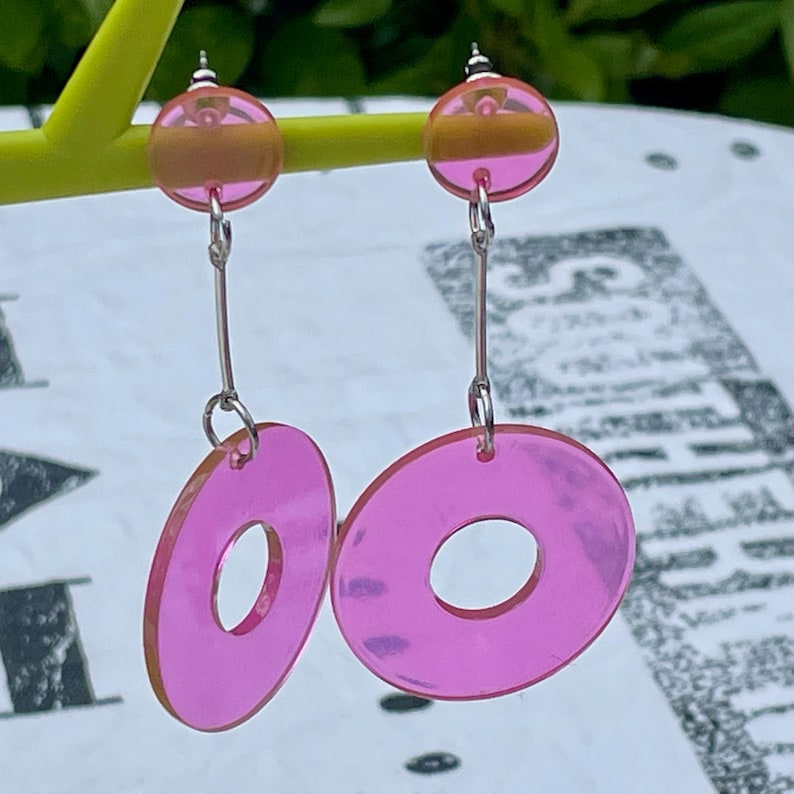 May include: Pink acrylic earrings with a donut shape and a smaller round bead at the top.