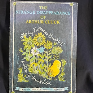 May include: Vintage hardcover book titled "The Strange Disappearance of Arthur Cluck." The cover features a dark blue background with yellow and green floral illustrations and a yellow bird. The author is Nathaniel Benchley, with pictures by Arnold Lobel.