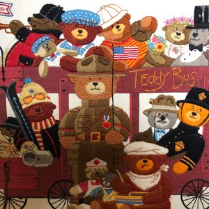 May include: A colorful embroidered picture of a teddy bear bus with various teddy bears dressed in different outfits. The bus is red with a wooden frame and wheels. The teddy bears are wearing hats, scarves, and other accessories. The text "Teddy Bus" is embroidered on the side of the bus.