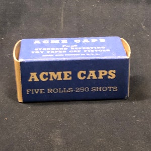 Op de afbeelding: Blauwe en gouden doos met Acme-capsules voor standaard herhalende speelgoed-papieren pistoolkappen. De doos heeft de tekst "Five Rolls - 250 Shots".