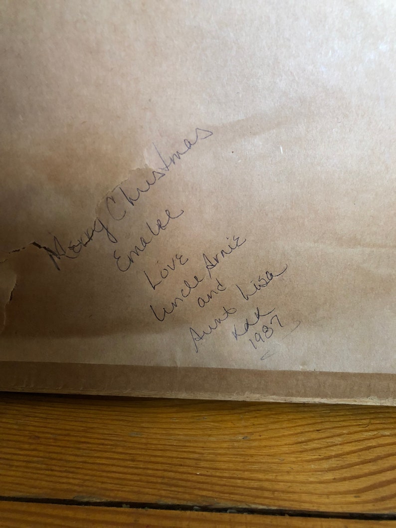 May include: A handwritten note on a brown paper background. The note says "Merry Christmas Emma Lee Love Uncle Arnie and his Aunt Kay 1987".