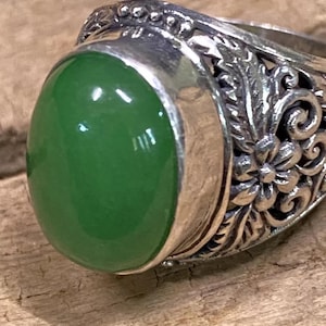 May include: A silver ring with a green gemstone set in a floral design.
