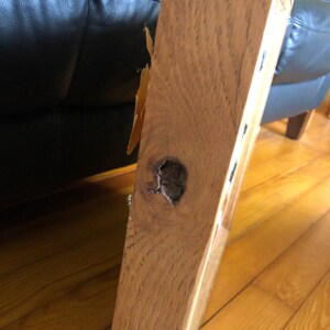 May include: Close-up of a wooden table leg with a knot hole. The wood is a light brown color and has a natural grain pattern.