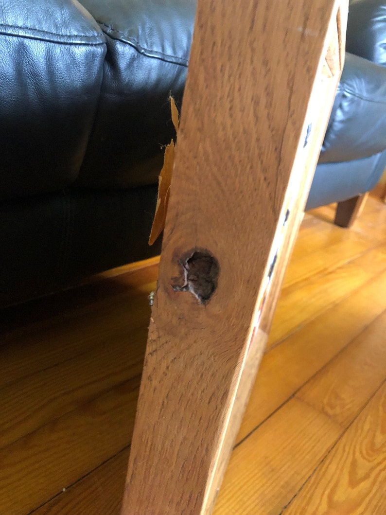 May include: Close-up of a wooden table leg with a knot hole. The wood is a light brown color and has a natural grain pattern.