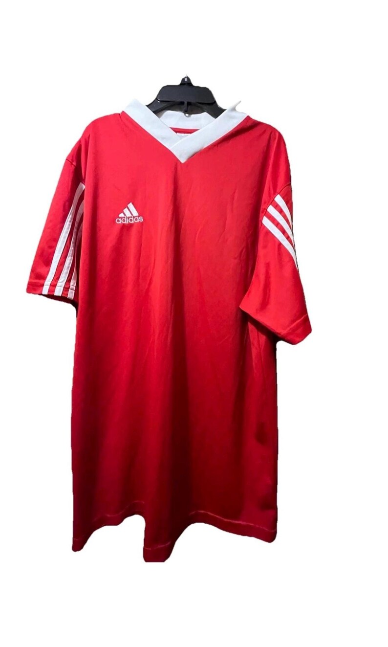 K&ouml;nnte beinhalten: Rotes Adidas Fu&szlig;balltrikot mit wei&szlig;en Akzenten. Mit V-Ausschnitt und Adidas-Logo auf der Brust. Wei&szlig;e Streifen auf den &Auml;rmeln. Ein klassisches Sport-Top.