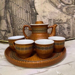 May include: A brown and black woven tea set with a teapot and four cups. The set is on a brown woven tray.