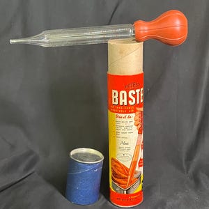 Könnte beinhalten: Vintage Küchenbaster-Set mit einem durchsichtigen Glasrohr und einem roten Gummiball. Das Set enthält eine Pappröhre mit dem Text "Artbeck Baste" und einen kleinen blauen Behälter. Der Baster ist zum Braten von Fleisch und Geflügel bestimmt.