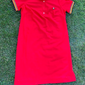May include: A red collared dress with a white collar and rainbow stripes on the collar and sleeves. The dress has a single button closure at the neck.