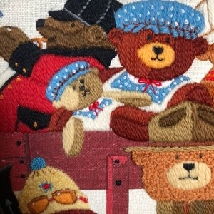 May include: Embroidered wall art featuring a group of teddy bears wearing different hats and outfits. The bears are arranged in a row, with the one in the front wearing a blue hat and a red bow tie. The bears are all smiling and looking at the viewer.