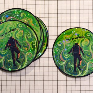 May include: A collection of round stickers featuring an astronaut figure against a swirling green and white background. The stickers have the text "I'll do my best." The astronaut is wearing a dark suit. The stickers have a glittery effect.