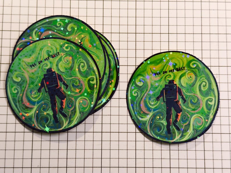 May include: A collection of round stickers featuring an astronaut figure against a swirling green and white background. The stickers have the text "I'll do my best." The astronaut is wearing a dark suit. The stickers have a glittery effect.