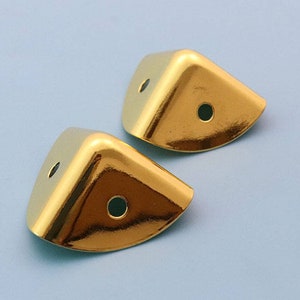 May include: Two gold corner protectors with a rounded edge and a hole in the center of each. The protectors are on a light blue background.