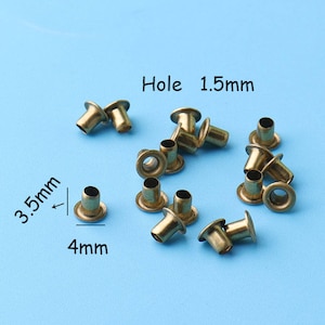 May include: A close-up of a group of 15 gold-colored metal eyelets. The eyelets have a 1.5 mm hole and are 3.5 mm in diameter. The eyelets are arranged in a semi-circle on a blue surface. The text "Hole 1.5mm" and "3.5mm" and "4mm" are visible in the image.