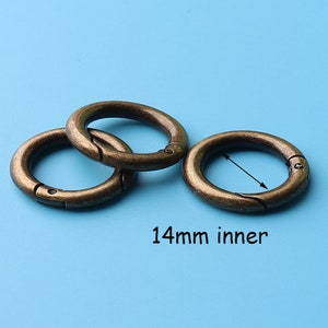 May include: Three antique gold-toned metal key rings with a 14mm inner diameter. The rings are open and have a spring-loaded closure.