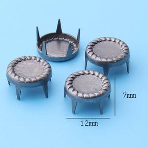 May include: Four silver metal furniture tacks with a 12 mm diameter and 7 mm height. The tacks have a decorative, circular design.