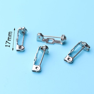 May include: Four silver-colored brooch pin backs, each with a safety pin style closure. One pin back measures 17mm in length. The pins are displayed on a light blue background.