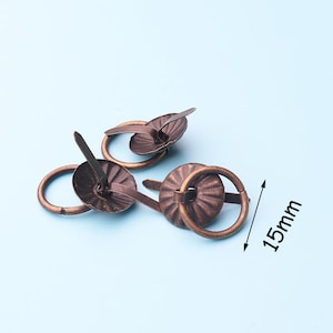 May include: Three antique bronze-colored ring pulls with a decorative fluted design. Each pull has a 1.5 inch diameter ring and a pointed nail for attaching to a surface.