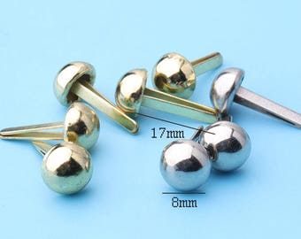May include: Assortment of gold and silver metal rivets with a 17 mm length and 8 mm diameter. The rivets have a pointed end and a flat head.