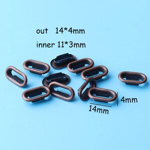 Op de afbeelding: Een close-up van 10 bronzen metalen oogjes. De oogjes zijn ovaalvormig met een buitendiameter van 14 mm en een binnendiameter van 11 mm. De tekst "out 14*4mm" en "inner 11*3mm" is zichtbaar in de afbeelding.
