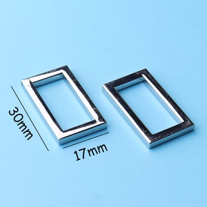 May include: Two silver metal rectangular rings, each with a 17 mm width and 30 mm length.