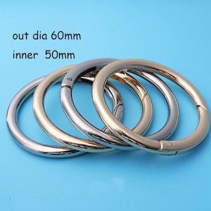 Puede incluir: Cuatro anillos metálicos, dos plateados y dos dorados, con un diámetro exterior de 60 mm y un diámetro interior de 50 mm. Los anillos están apilados uno encima del otro.