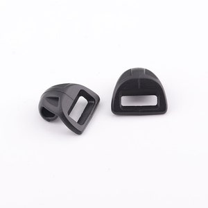 May include: Two black plastic slider buckles for straps or belts. The buckles are designed to be used with webbing or straps.