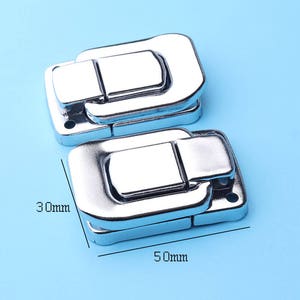 Puede incluir: Dos cierres de metal plateados con un cierre de resorte. Los cierres miden 7,6 cm de largo y 12,7 cm de ancho.