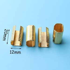 May include: Four gold-colored metal clasps, each measuring 12 mm wide and 20 mm long. The clasps have a ribbed design and are ideal for attaching to fabric or other materials.