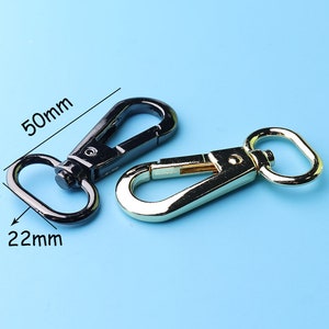 Peut inclure: Deux fermoirs métalliques, l'un noir et l'autre doré, mesurant 50 mm de long et 22 mm de large. Les fermoirs sont conçus pour être fixés à des sacs, des sangles ou d'autres articles.