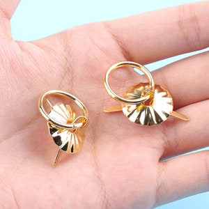 Może przedstawiać: Dwa złote metalowe uchwyty w kształcie pierścienia z ozdobnym, żebrowanym wzorem. Uchwyty są przymocowane do metalowego kołka.