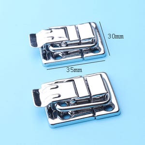 Puede incluir: Dos cierres de caja de metal plateados con un cierre de resorte. Cada cierre mide 8,9 cm por 7,6 cm.