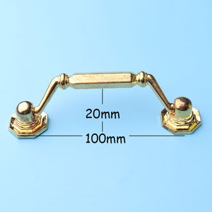 May include: Gold-toned metal cabinet pull with a 100mm length and 20mm width. The pull has a rounded, decorative end on each side.