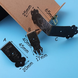 May include: Three antique-style metal corner brackets with intricate floral designs. The brackets are 40mm, 45mm, and 65mm in length. They are a dark bronze color.