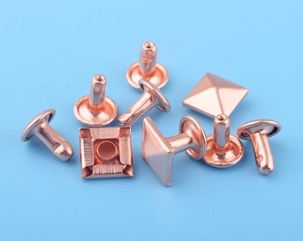 May include: Assortment of rose gold metal rivets, including square and pyramid shapes, with some having a post and others having a flat base.