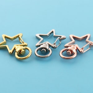 May include: Three star-shaped keyrings with swivel clasps. The keyrings are gold, silver, and rose gold.