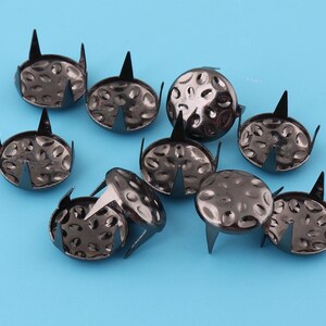 May include: A group of ten black metal nailheads with a decorative pattern on the top. The nailheads have four sharp points on the bottom.