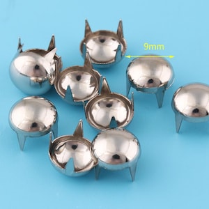 May include: Nine silver metal studs with a 9mm diameter. Each stud has four prongs on the bottom.