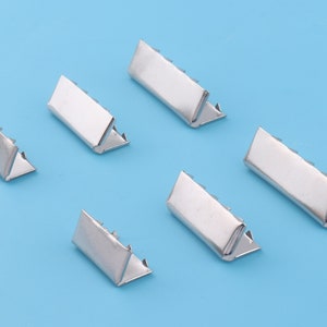 Puede incluir: Seis hebillas deslizantes de metal plateado, cada una con forma rectangular y extremo puntiagudo. Las hebillas están dispuestas de forma dispersa sobre un fondo azul claro.