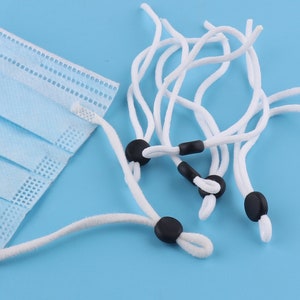May include: White elastic cords with black adjustable toggles. The cords are used for face masks.