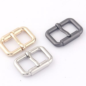 May include: Three metal belt buckles in different finishes: gold, silver, and gunmetal. Each buckle has a rectangular shape with a smooth, polished surface.