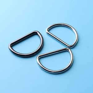 May include: Three metal D-rings, two silver and one black, on a light blue background.