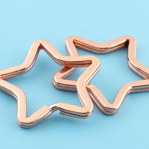 Può includere: Due portachiavi a forma di stella color oro rosa, uno leggermente più grande dell'altro, sono impilati uno sopra l'altro.