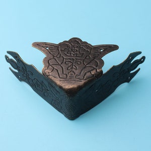 May include: Antique brass corner bracket with a decorative design featuring two cherubs with wings and floral accents.