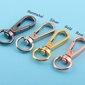 Può includere: Quattro portachiavi in metallo in diverse finiture: canna di fucile, argento, oro e oro rosa. Ogni portachiavi ha un gancio girevole e un anello rotondo.