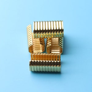 May include: Four gold metal cord end caps with a ribbed design. The caps are stacked on top of each other.
