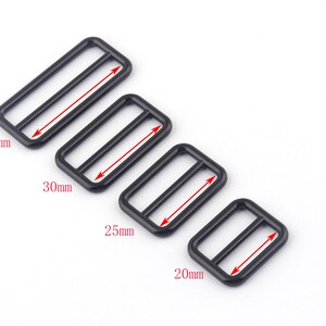 May include: Four black metal slider buckles in different sizes: 38mm, 30mm, 25mm, and 20mm. The buckles are rectangular with a center opening and two parallel lines.