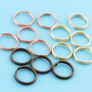 May include: Assortment of key rings in three different colours: copper, gold, and bronze. The key rings are all double-looped and are arranged in a semi-circle on a blue background.