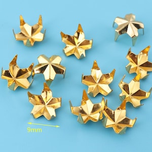May include: Ten gold-colored metal star-shaped studs, each with six points, measuring 9mm in diameter. The studs are scattered on a light blue background.